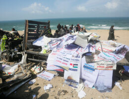 Palestinians inspect the remains of a heavily damaged humanitarian aid vehicle destroyed by Israeli airstrikes. The airstrike also killed nine Palestinians and injured dozens, in Deir al-Balah, Gaza on March 3, 2024. (Photo: Ramadan El-Agha/APA Images)