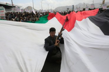 An Ansar Allah supporter holds a weapon through the gap of a large-scale Palestinian flag during a protest against the US and Israel and in support of Palestinians, in Sana'a, Yemen, on March 1, 2024. (Photo: © Yahya Arhab/EFE via ZUMA Press APAimages)