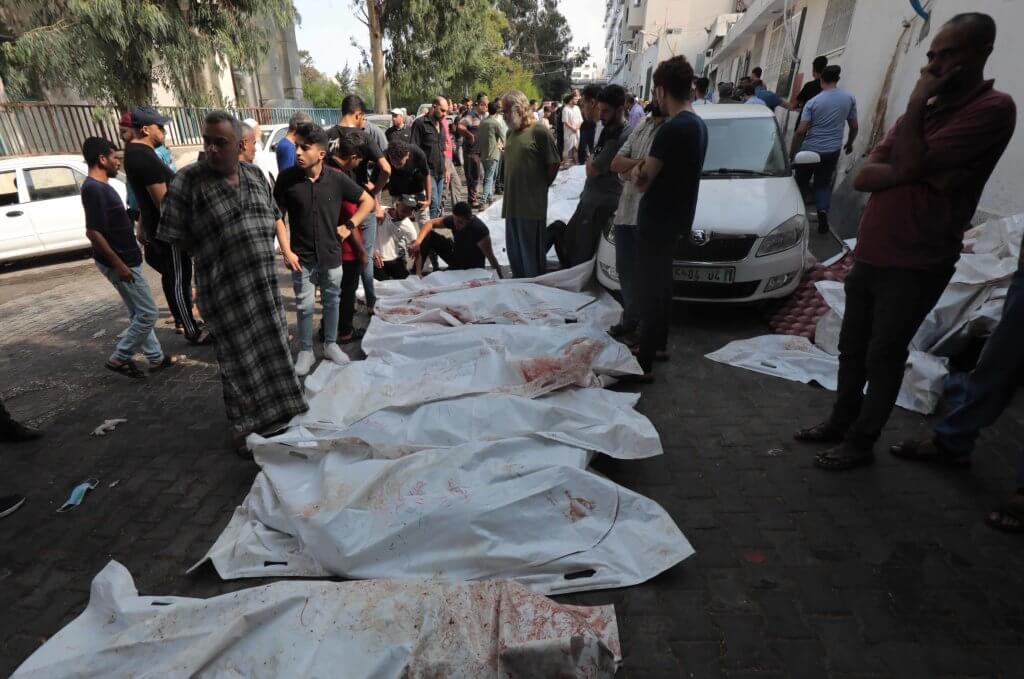 People stand by the bodies of victims of Israeli airstrikes outside the morgue of al-Shifa hospital in Gaza City on October 12, 2023. (Photo: Naaman Omar/APA Images)