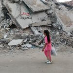 Girl walks past a destroyed building in Gaza City, with graffiti on the ruins saying, "We promise to rebuild," May 29, 2024. (Photo: Khaled Daoud/APA Images)