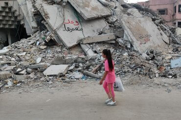Girl walks past a destroyed building in Gaza City, with graffiti on the ruins saying, "We promise to rebuild," May 29, 2024. (Photo: Khaled Daoud/APA Images)