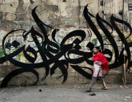 A woman walks by a wall a graffiti mural by Palestinian artist Bilal Khaled in Beirut's Burj al-Barajneh refugee camp that says "In the name of the camp, I did not die and ask Jenin," on June 10, 2022. (Photo: Nidal Al-Wahidi/APA Images)