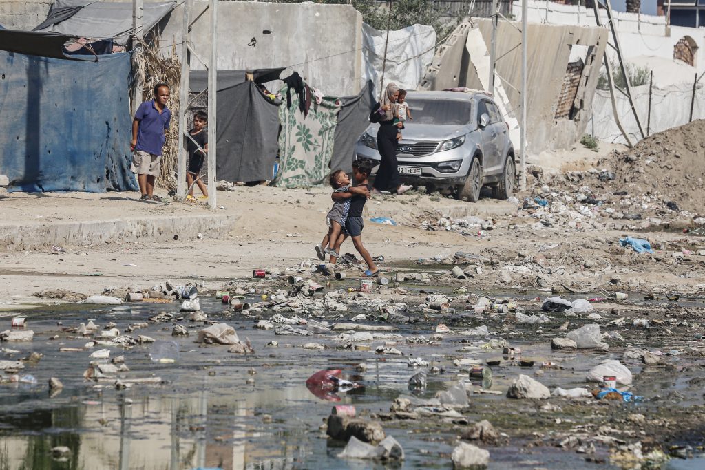 Palestinian children play next to a tent camp filled with displaced Palestinian families in the central Gaza Strip. The streets are covered in stagnant water and trash, which health officials say poses a major risk to public health.