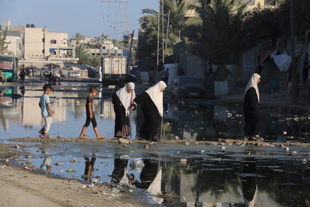 Palestinians walk amid overflowing sewage in a displacement camp in Deir al-Balah, central Gaza, August 24, 2024. (Photo: Omar Ashtawy/APA Images)