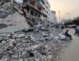 Palestinians walk in front of graffiti written in Arabic: "We will rebuild Gaza" on the wall of a building destroyed during Israeli attacks, in Gaza City on May 29, 2024. (Photo by Khaled Daoud/APA Images)