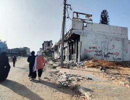 Palestinians walk in front of graffiti written in Arabic: "We promise, we will rebuild Gaza" on the wall of a building destroyed during an Israeli attack, Gaza City, May 29, 2024. (Photo: Khaled Daoud/APA Images)