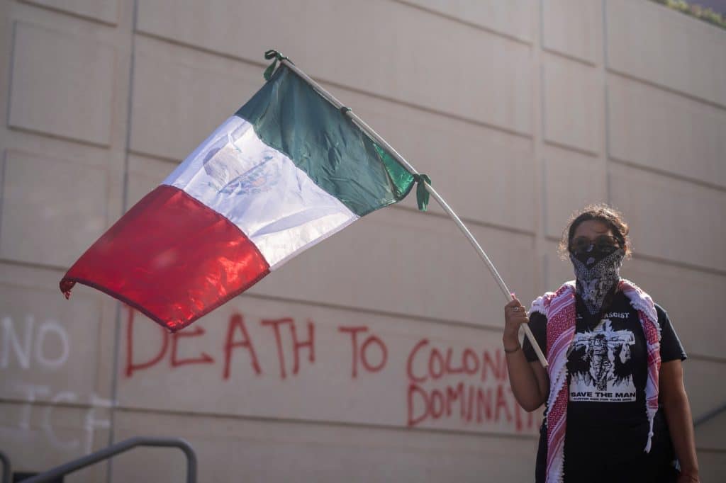 A demonstrator wearing a Palestinian keffiyeh holds a Mexican flag at a protest outside the Federal Building following an immigration enforcement operation by federal authorities on Friday, June 6, 2025, in Los Angeles. (Photo: Ringo Chiu / Shutterstock.com)