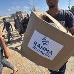 Palestinians aid-seekers carrying Rahma Worldwide aid boxes from an aid distribution site run by the U.S.-backed Gaza Humanitarian Foundation, in Rafah, southern Gaza. May 27, 2025. The boxes were distributed at the GHF site without the knowledge or consent of Rahmah Worldwide, according to the organization's Director, who spoke to Mondoweiss. (Photo: Ahmed Ibrahim/APA Images)