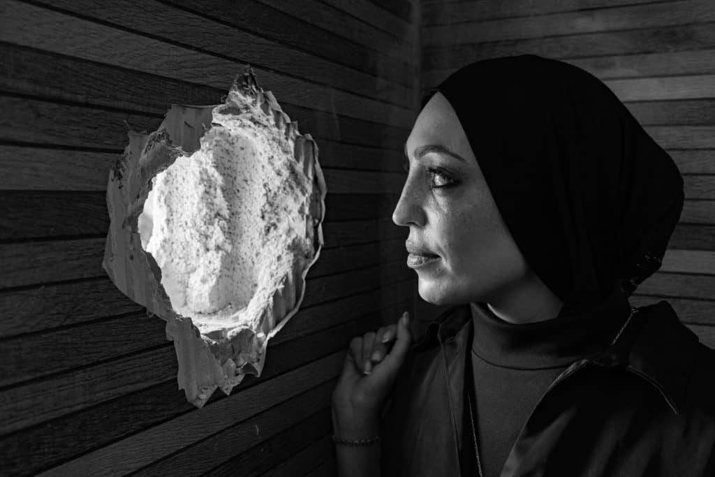 During a 10-day raid on the Jenin refugee camp in the summer of 2024, Israeli soldiers used Alaa Pwaqneh's family home as a base for their military operations. While the family was forced to remain in one room, the army climbed to the upper floor and dug a hole in the bathroom wall for a sniper to use. Alaa poses for a portrait where the sniper hole was used in her home. On November 9, Tamam Mar’i was in the house with her son, daughter-in-law and their two children when the army invaded Jenin. Her husband was out buying groceries when the army came, and couldn’t return home. The army, looking for armed militants, bombed their home with a rocket launcher, and the family entered the back room, hoping to not be killed from that blast. Tamam finally went outside to explain to the army that no militants are inside her home. The army escorted all the family outside, handcuffed her son, and bombed her home again. Tamam and her husband pose for a portrait in their destroyed home. (Photo: David Lombeida)