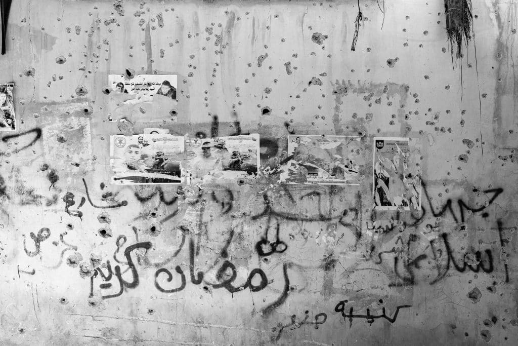 Posters of resistance fighters killed in Jenin can be seen on a wall in Jenin refugee camp. Many walls are covered in bullet holes from raids in Jenin refugee camp. Israeli soldiers also deface posters of fighters when they occupy the camp. (Photo: David Lombeida)