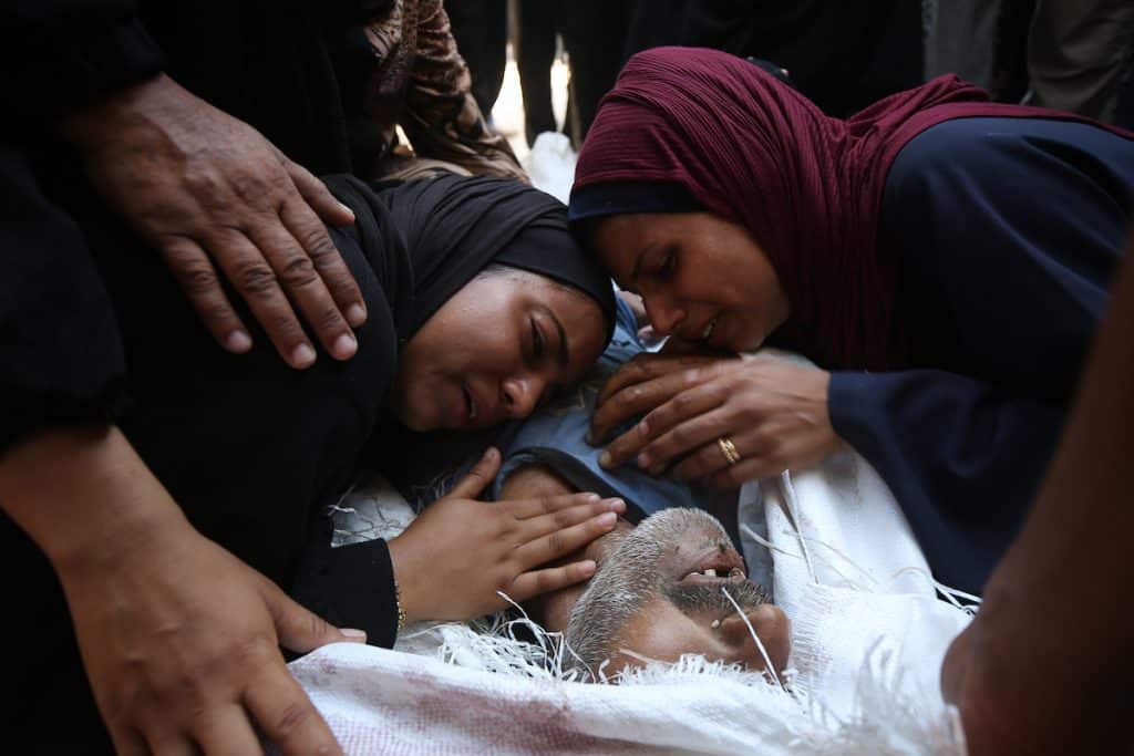 Palestinians mourn over the bodies of loved ones who were killed by Israeli fire while trying to receive aid, according to medics, at Al-Shifa Hospital, in Gaza City, August 4, 2025. (Photo by Omar Ashtawy/APA Images)