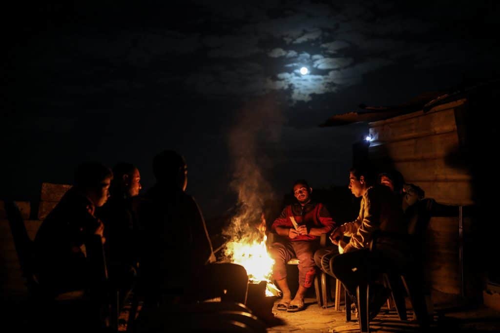 Palestinians go about their daily lives at night in tents set up atop the rubble of destroyed buildings in the Sheikh Radwan neighborhood of central Gaza City, on December 5, 2025. (Photo: Omar Ashtawy/APA Images)