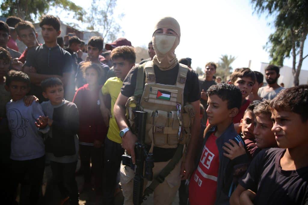 Palestinian militants of the Izz al-Din al-Qassam Brigades, the military wing of Hamas, stand guard next to a crowd watching the transfer of released Israeli hostages to the Red Cross in the south of Deir el-Balah in the central Gaza Strip, October 13, 2025. (Photo: Omar Ashtawy/APA Images)