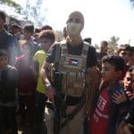 Palestinian militants of the Izz al-Din al-Qassam Brigades, the military wing of Hamas, stand guard next to a crowd watching the transfer of released Israeli hostages to the Red Cross in the south of Deir el-Balah in the central Gaza Strip, October 13, 2025. (Photo: Omar Ashtawy/APA Images)