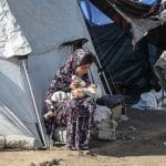 A Palestinian woman bottle feeds a baby outside a tent in a displacement camp in Gaza