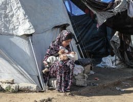 A Palestinian woman bottle feeds a baby outside a tent in a displacement camp in Gaza