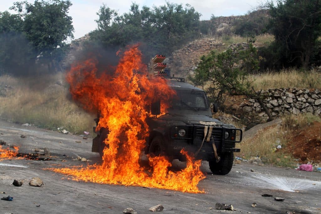 Un vehículo militar israelí envuelto en llamas después de que jóvenes palestinos lanzaran bombas molotov contra las fuerzas israelíes durante una protesta conmemorativa del Día de la Nakba frente a la prisión militar de Ofer, en las afueras de Ramallah, el 15 de mayo de 2013. (Foto: Issam Rimawi/APA Images)
