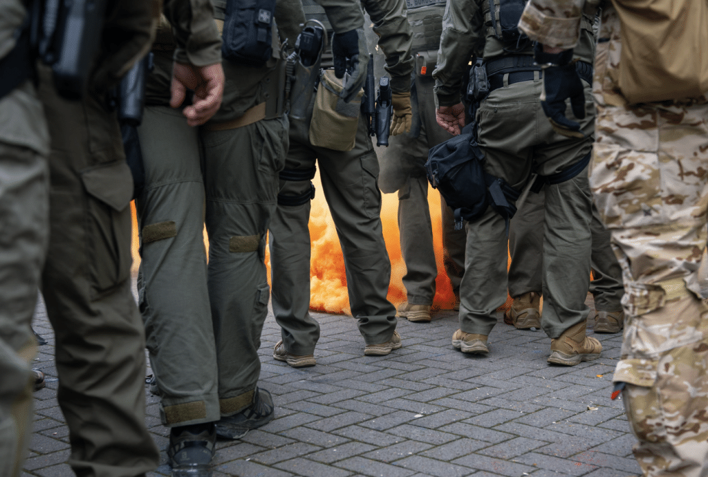 Federal officers from the U.S. Bureau of Prisons, U.S. Customs and Border Protection, U.S. Border Patrol, Homeland Security Investigations and U.S. Immigration and Customs Enforcement prepare to provide security amid a haze of CS gas used to disperse protesters outside the ICE facility in Portland, Oregon on October 4, 2025 (Flickr)