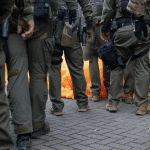 Federal officers from the U.S. Bureau of Prisons, U.S. Customs and Border Protection, U.S. Border Patrol, Homeland Security Investigations and U.S. Immigration and Customs Enforcement prepare to provide security amid a haze of CS gas used to disperse protesters outside the ICE facility in Portland, Oregon on October 4, 2025 (Flickr)