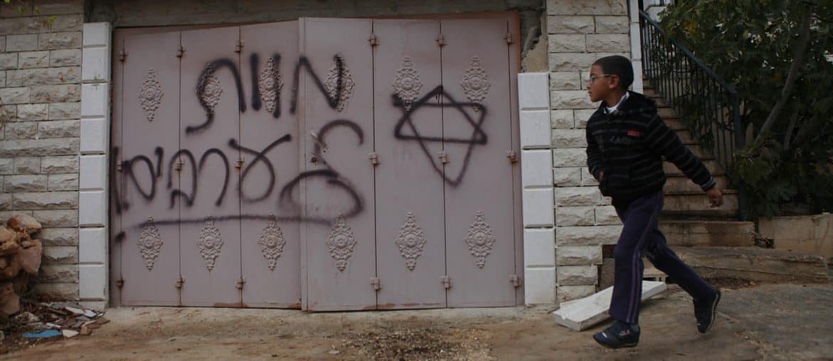 A Palestinian boy walks past Hebrew grafitti that reads "Death to Arabs" written by Israeli settlers on the door of the Hamayel family home in the Palestinian village of Abu Falah, northeast of Ramallah, November 23, 2014. (Photo: Shadi Hatem/APA Images)