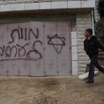 A Palestinian boy walks past Hebrew grafitti that reads "Death to Arabs" written by Israeli settlers on the door of the Hamayel family home in the Palestinian village of Abu Falah, northeast of Ramallah, November 23, 2014. (Photo: Shadi Hatem/APA Images)