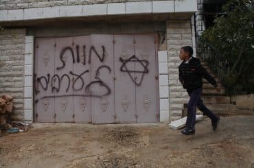 A Palestinian boy walks past Hebrew grafitti that reads "Death to Arabs" written by Israeli settlers on the door of the Hamayel family home in the Palestinian village of Abu Falah, northeast of Ramallah, November 23, 2014. (Photo: Shadi Hatem/APA Images)