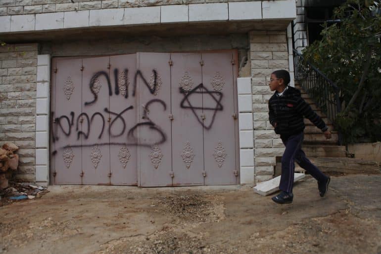 A Palestinian boy walks past Hebrew grafitti that reads "Death to Arabs" written by Israeli settlers on the door of the Hamayel family home in the Palestinian village of Abu Falah, northeast of Ramallah, November 23, 2014. (Photo: Shadi Hatem/APA Images)