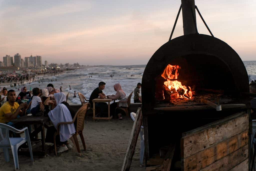People sit by a beachside grill as food is prepared along Gaza’s shore in the evening, July 11, 2022. (Photo: Mahmoud Nasser)