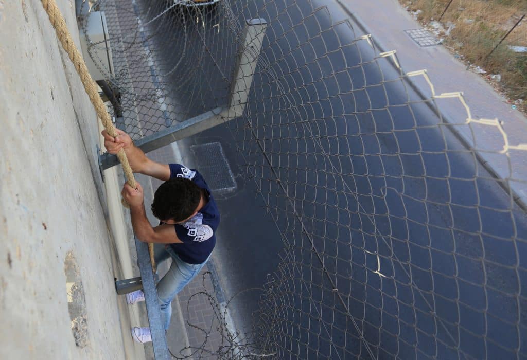 Palestinians who had been prevented from crossing through the Qalandia checkpoint into Jerusalem jump over the separation wall in the town of al-Ram, north of Jerusalem, June 18, 2015. (Photo: Shadi Hatem/APA Images)