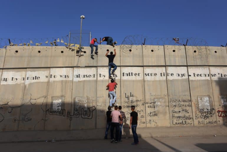 Palestinians who had been prevented from crossing through the Qalandia checkpoint into Jerusalem use a ladder to cross over the separation wall in the town of al-Ram, north of Jerusalem, June 18, 2015. (Photo: Shadi Hatem/APA Images)