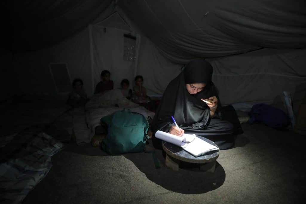 Dana Mohammed Abu Dalfa, a Palestinian high school student, reviews her lessons using the light of a mobile phone inside a displacement tent in the Gaza Strip, June 20, 2026. (Photo: Hassan Jedi /APA Images)