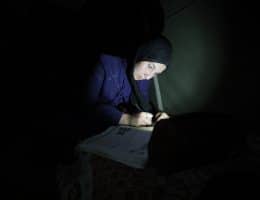 Dana Mohammed Abu Dalfa, a Palestinian high school student, reviews her lessons using the light of a mobile phone inside a displacement tent in the Gaza Strip, June 20, 2026. (Photo: Hassan Jedi /APA Images)