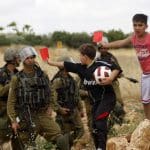 Palestinian children hold red cards in front of Israeli security forces during a demonstration against the Israeli Football Federation, in the West Bank village of Nabi Saleh, near Ramallah, May 29, 2015. (Photo by Shadi Hatem/APA images)