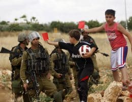 Palestinian children hold red cards in front of Israeli security forces during a demonstration against the Israeli Football Federation, in the West Bank village of Nabi Saleh, near Ramallah, May 29, 2015. (Photo by Shadi Hatem/APA images)