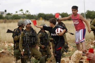 Palestinian children hold red cards in front of Israeli security forces during a demonstration against the Israeli Football Federation, in the West Bank village of Nabi Saleh, near Ramallah, May 29, 2015. (Photo by Shadi Hatem/APA images)