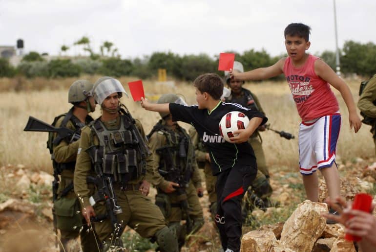 Palestinian children hold red cards in front of Israeli security forces during a demonstration against the Israeli Football Federation, in the West Bank village of Nabi Saleh, near Ramallah, May 29, 2015. (Photo by Shadi Hatem/APA images)