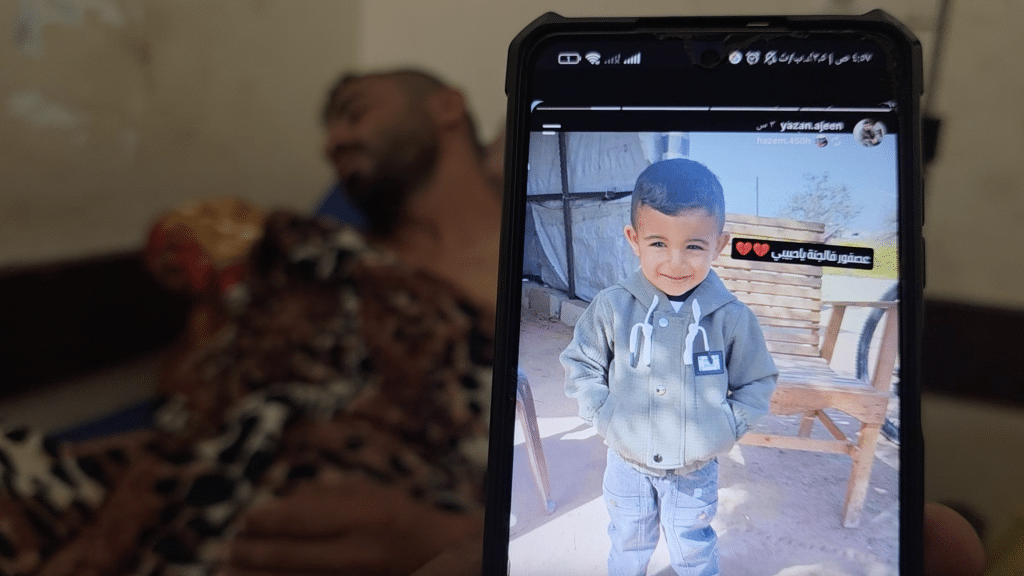 Bahaha Abu al-Ajeen at al-Aqsa Martyrs Hospital with a photo of his son, Rayyan. (Photo: Screenshot from video testimony gathered by Osama Kahlout for Mondoweiss)