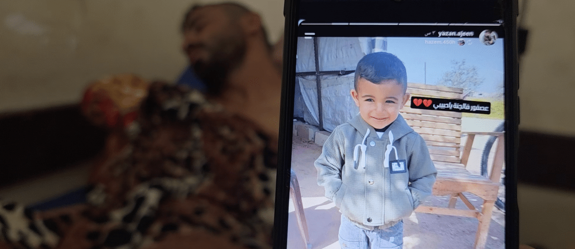 Bahaha Abu al-Ajeen at al-Aqsa Martyrs Hospital with a photo of his son, Rayyan. (Photo: Screenshot from video testimony gathered by Osama Kahlout for Mondoweiss)