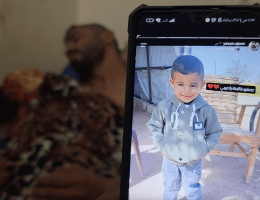 Bahaha Abu al-Ajeen at al-Aqsa Martyrs Hospital with a photo of his son, Rayyan. (Photo: Screenshot from video testimony gathered by Osama Kahlout for Mondoweiss)