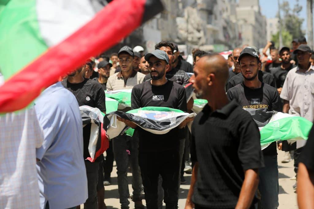Palestinians attend the funeral of 112 members of the Hassayna and Abu Sharia clans, who were killed in an Israeli strike in November 2023 during the beginning of the Gaza genocide. They were laid to rest on August 4, 2026, after their remains were recovered from underneath the rubble, nearly three years later. (Photo: Bilal Osama/APA Images)