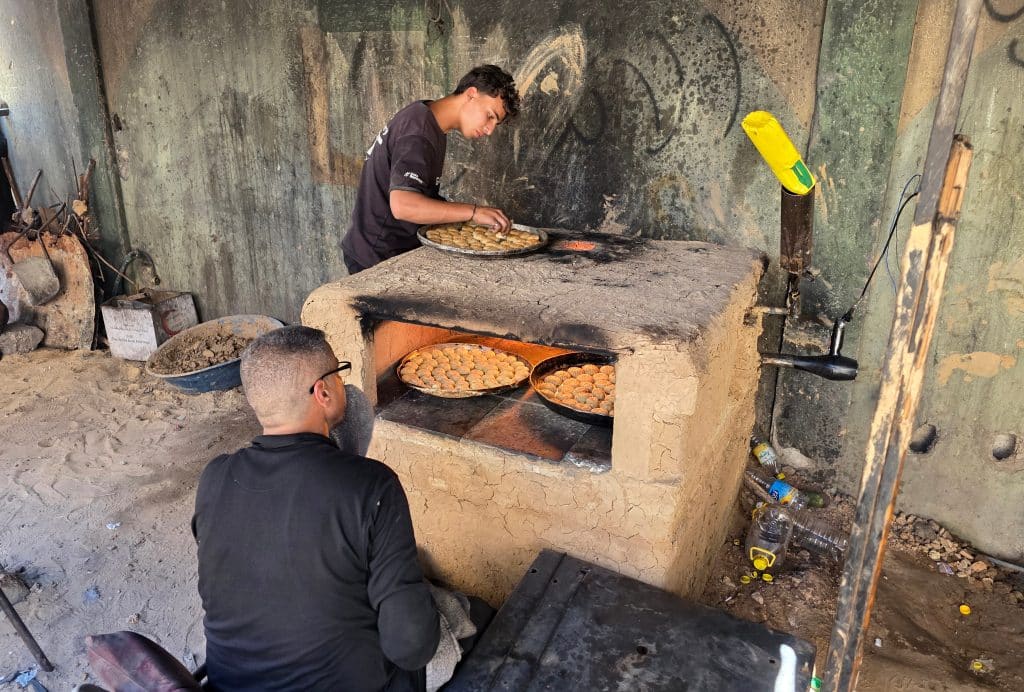 A displaced Palestinian family prepares and bakes traditional Eid cakes in a makeshift clay oven at a shelter center in Khan Younis, May 26, 2026. (Photo: Tariq Mohammad/APA Images)