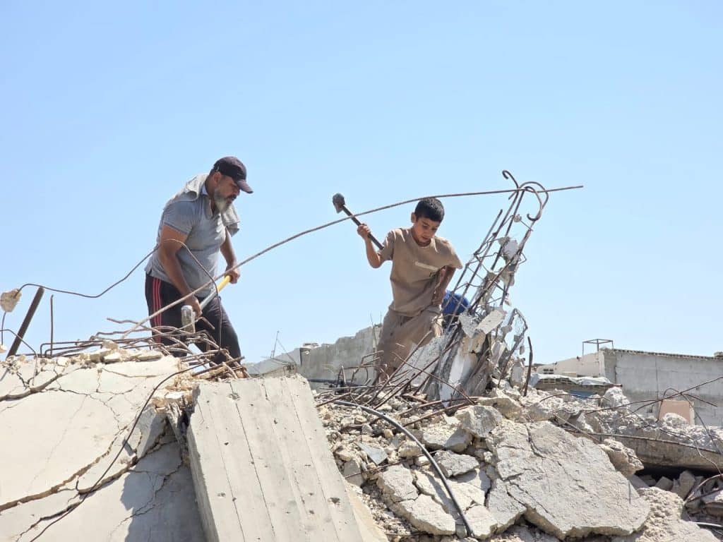 Khalil Abu Awda and his sons, Abdul Rahman, 14, and Muhammad, 16, work together to clear the rubble of their destroyed home so they can move from the al-Mawasi displacement camp in Khan Younis to their land. (Photo: Muhammad Eslayeh)