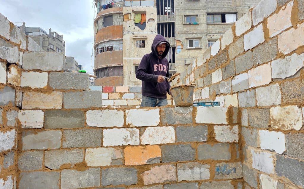 Palestinian shop owners in Khan Younis in southern Gaza remove debris by hand and rebuild their damaged stores using stones and red clay, December 27, 2025. (Photo: Tariq Mohammad/APA Images)