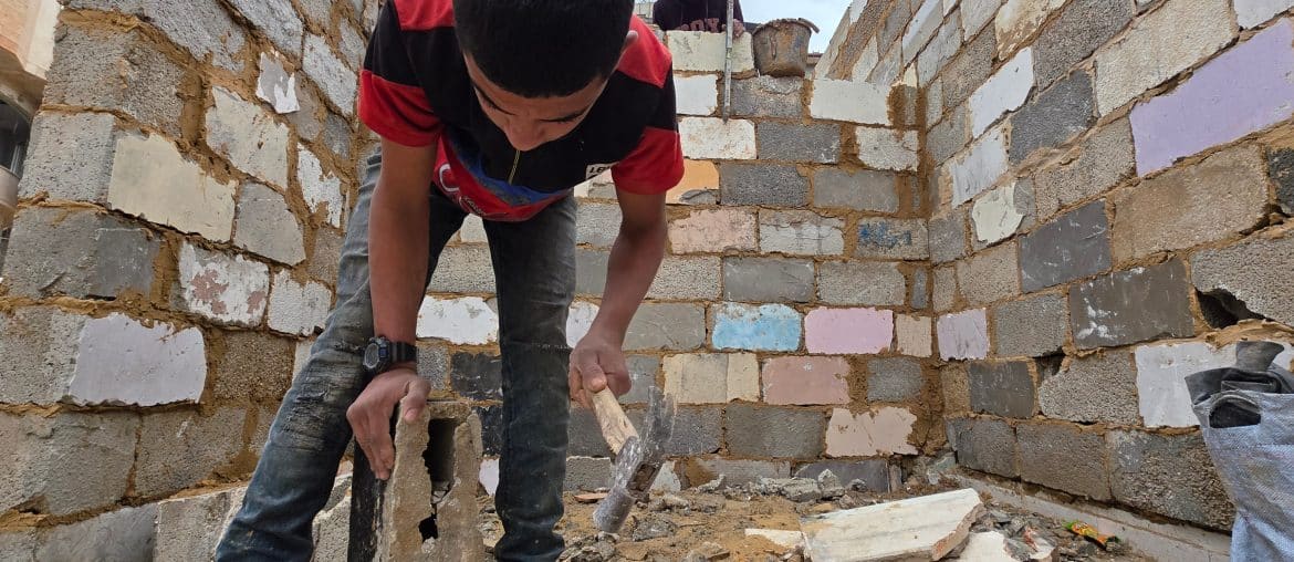Palestinian shop owners in Khan Younis in southern Gaza remove debris by hand and rebuild their damaged stores using stones and red clay, December 27, 2025. (Photo: Tariq Mohammad/APA Images)