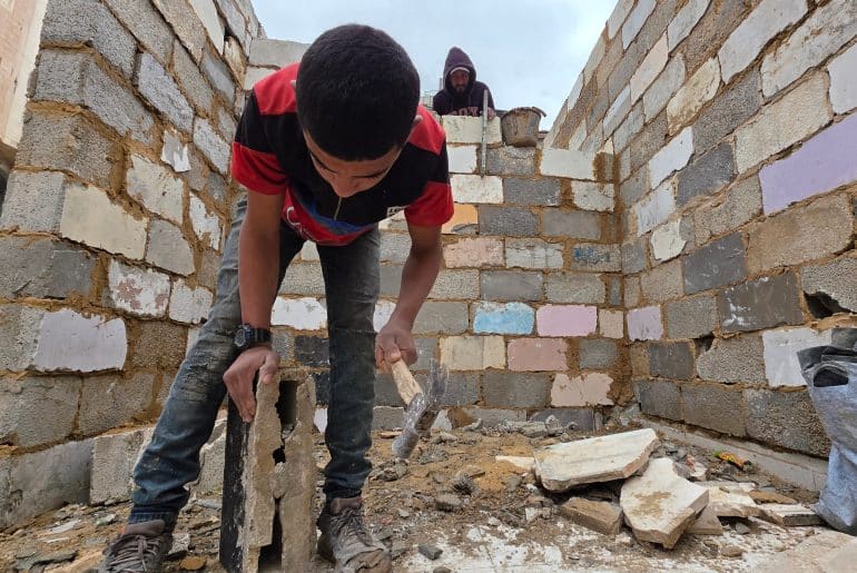 Palestinian shop owners in Khan Younis in southern Gaza remove debris by hand and rebuild their damaged stores using stones and red clay, December 27, 2025. (Photo: Tariq Mohammad/APA Images)