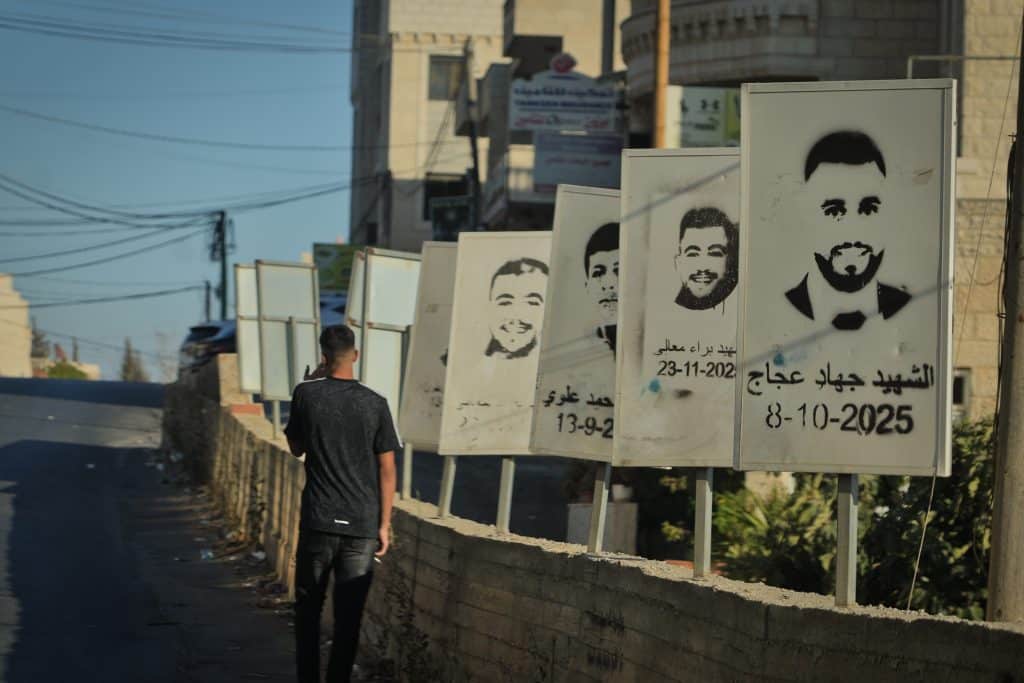 A Palestinian teenager walks past stenciled images of Deir Jarir martyrs slain by the Israeli army or settlers in Deir Jarir. (Photo: Qassam Muaddi/Mondoweiss)