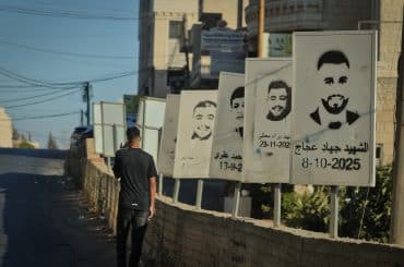A Palestinian teenager walks past stenciled images of Deir Jarir martyrs slain by the Israeli army or settlers in Deir Jarir. (Photo: Qassam Muaddi/Mondoweiss)