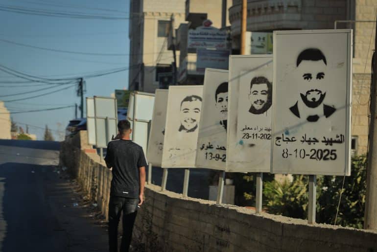 A Palestinian teenager walks past stenciled images of Deir Jarir martyrs slain by the Israeli army or settlers in Deir Jarir. (Photo: Qassam Muaddi/Mondoweiss)